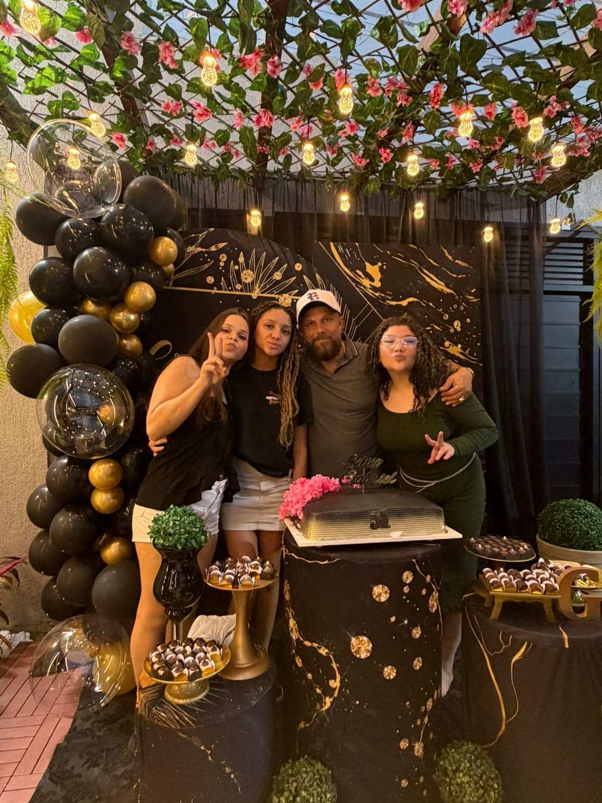 Família reunida em frente à mesa do bolo decorada em preto e dourado