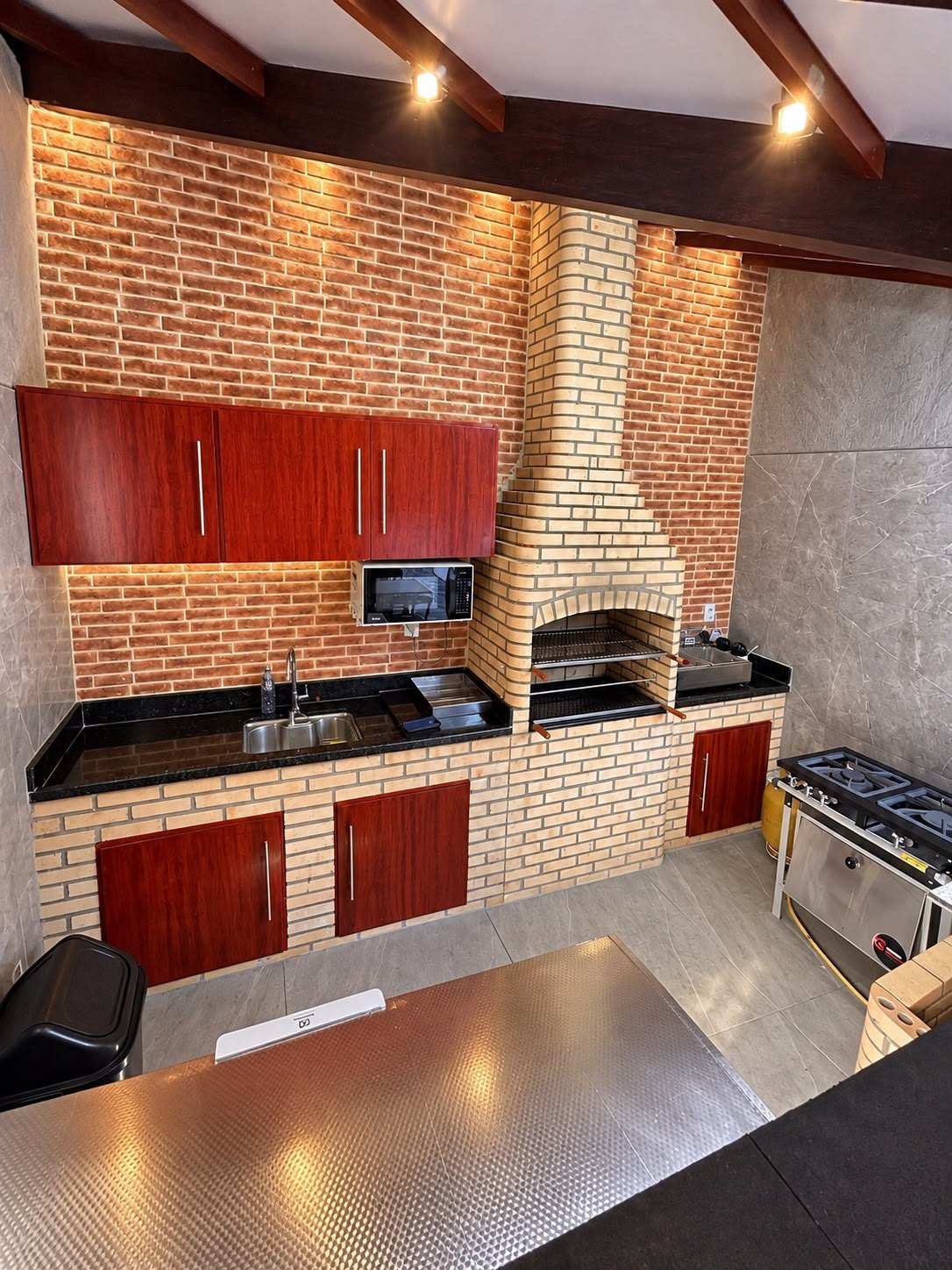 Cozinha com churrasqueira de tijolinho, armários, pia com bancada de granito, micro-ondas e fogão industrial