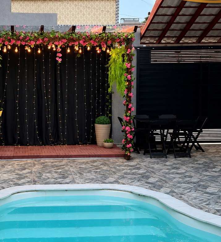 Pergolado com flores e cortina de luzes reservado para a mesa do bolo, em frente à piscina